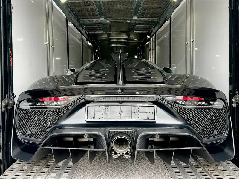Rear view of a sleek, black sports car with aerodynamic design, parked inside a trailer, highlighting its exhaust and taillights.