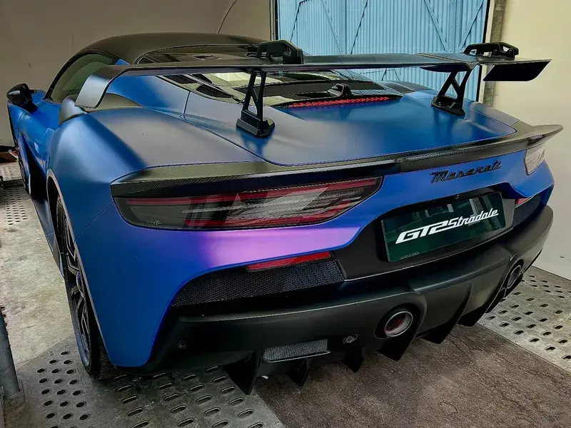 Blue Maserati GT2 Stradale with a prominent rear wing, parked in a garage, showcasing its sleek design and sporty features.
