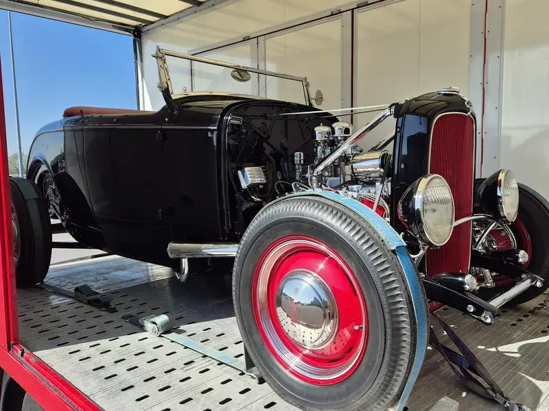 Vintage black convertible car with red wheels on a trailer, showcasing a polished engine and classic design elements.